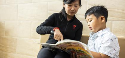 little boy reading book with educator