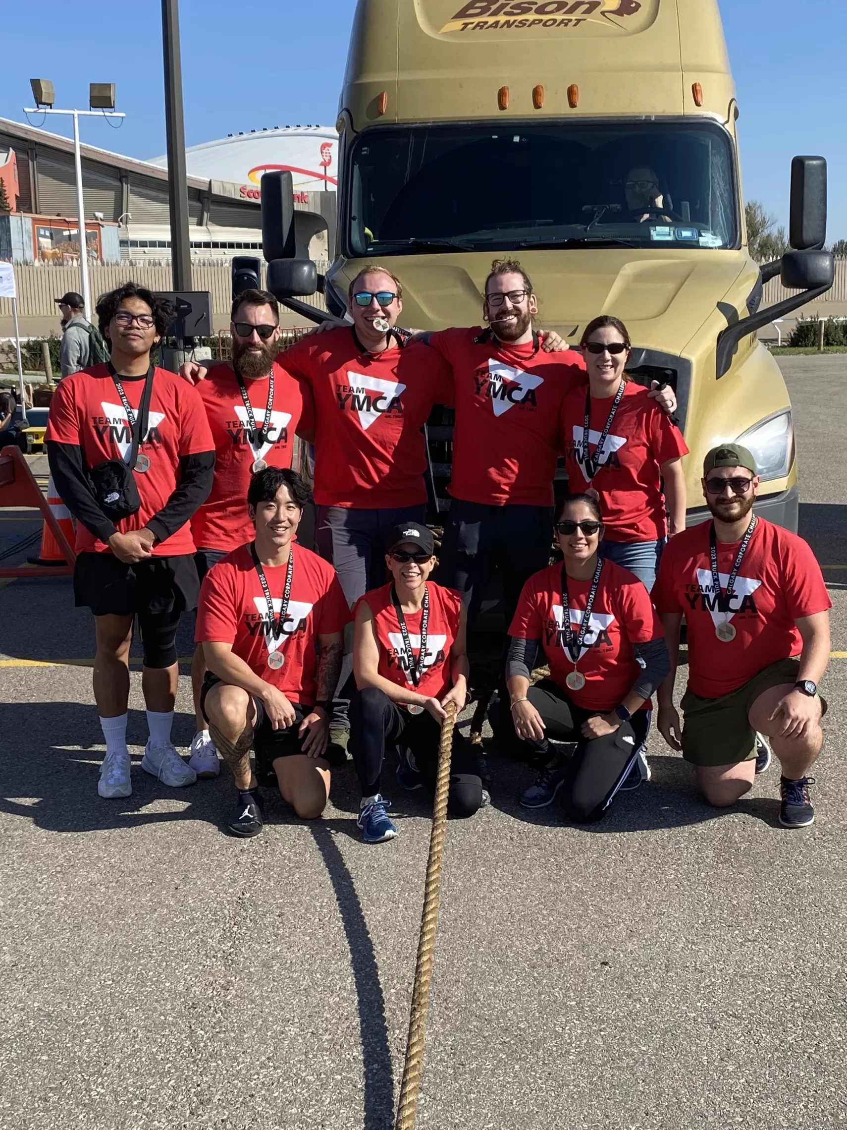 Team YMCA poses in front of a semi truck for the truck pull challenge through Calgary Corporate Challenge.