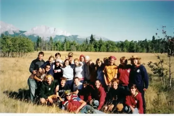 A group of campers at Camp Chief Hector YMCA pose in a field on a sunny day with the mountains spanning the background.