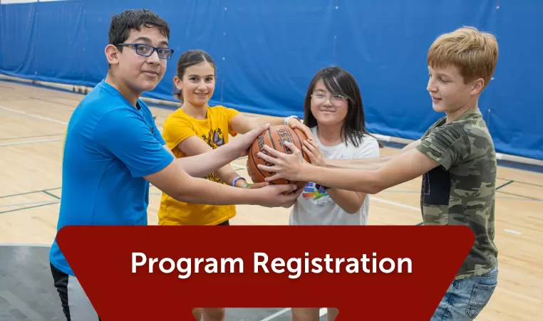 4 youth hold onto a basketball together, smiling and enjoying their time at the YMCA. The header says Program Registration on a dark red triangle graphic.