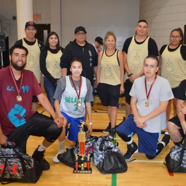 A group of youth pose for a photo amongst trophies at the 15th Annual Indigenous Hoops Tournament at YMCA Calgary in 2018