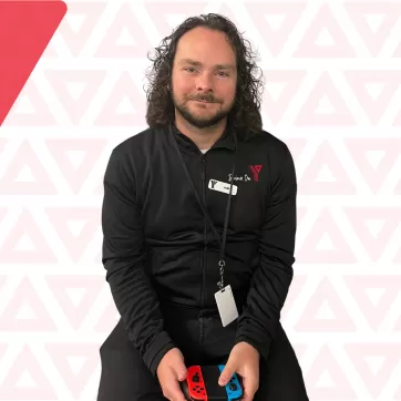 Kurt Robertson, YMCA Calgary Esports Supervisor, smiling while holding a gaming controller 