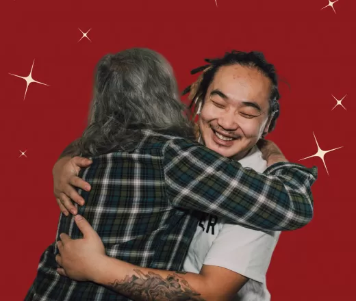 Two people hug, the one facing the camera smiles