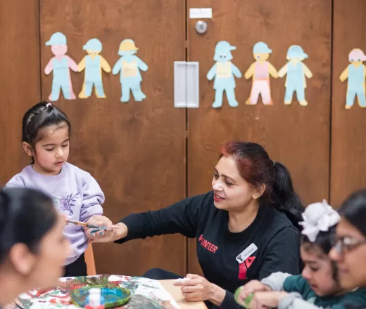 A volunteer helps children in the preschool room make crafts at Saddletowne YMCA