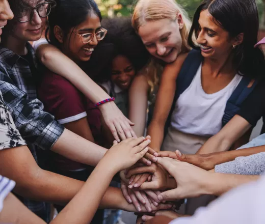 Youth gather around and place their hands together