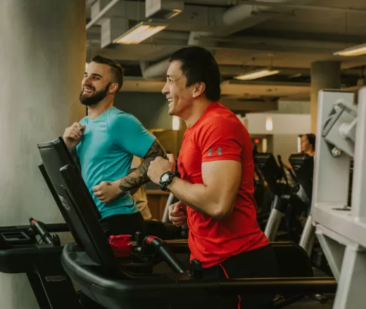 Two adult men run on treadmills