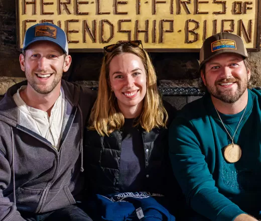 Three friends sit in front of the iconic fireplace at Hector Lodge