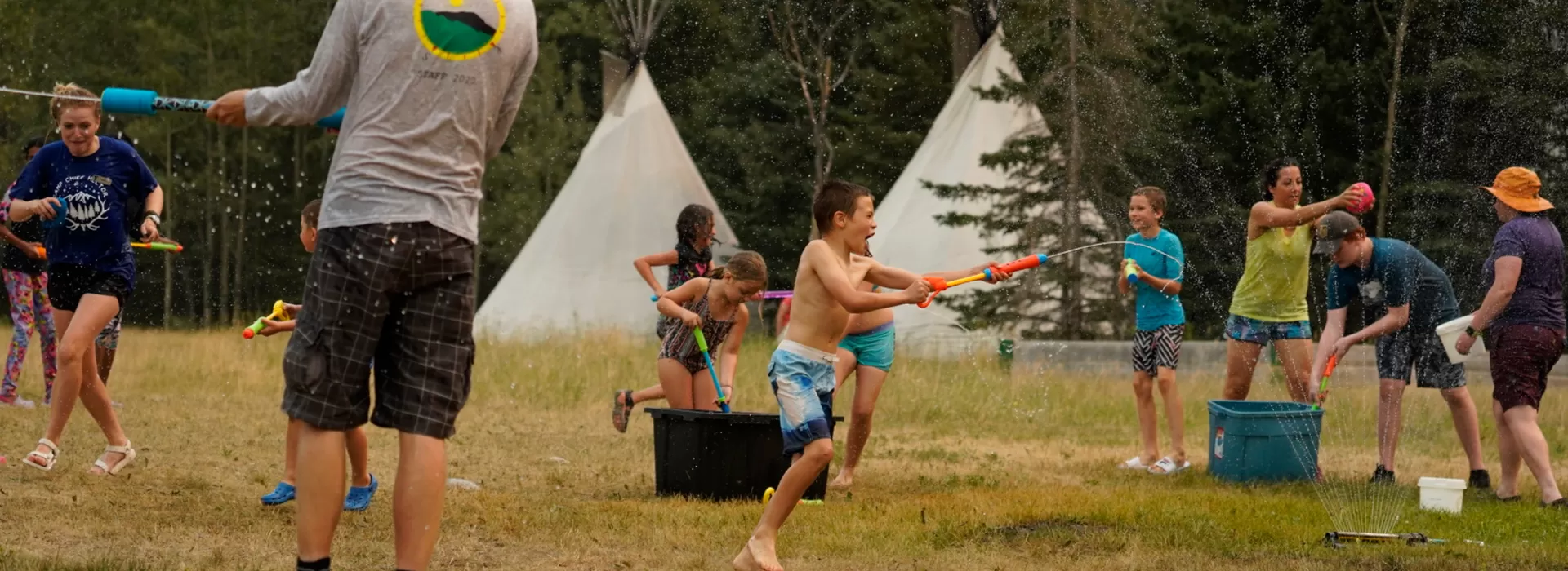 Families having a water fight in front of tipis