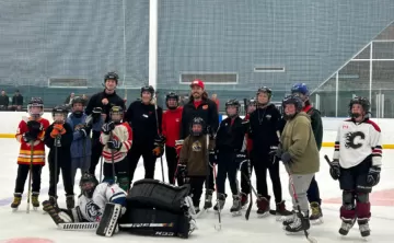Group of youth wearing hockey gear on the ice smiling with Calgary Flames Forward, Ryan Lomberg